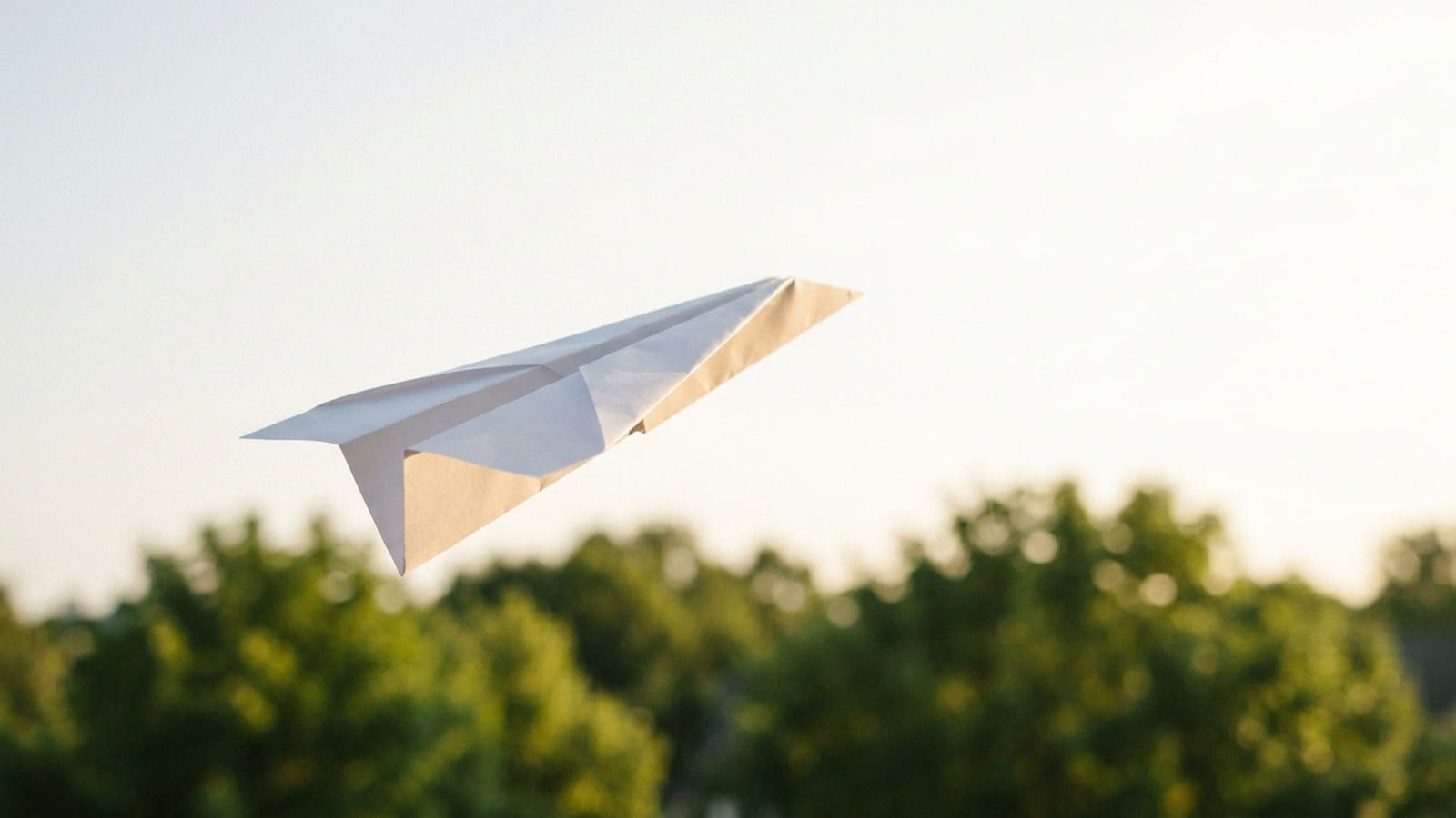 Weißer Papierflieger im Flug vor hellem Himmel